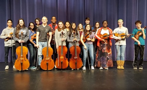 Students standing on a stage with orchestra instruments