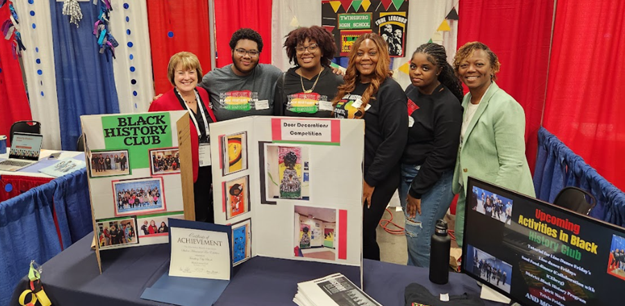 superintendent, club advisor and students in front of Black History Booth